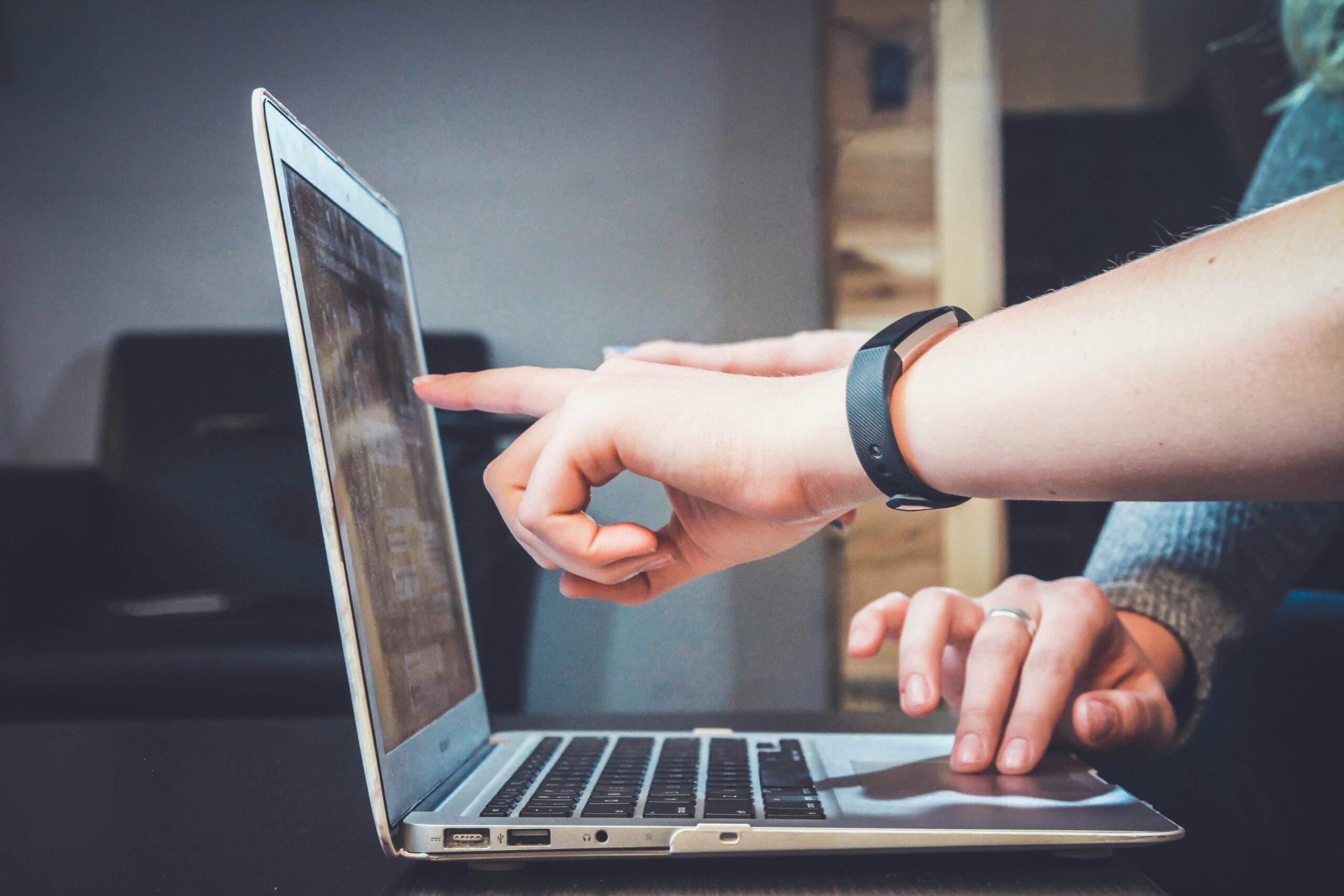 dłoń pokazująca coś na ekranie laptopa